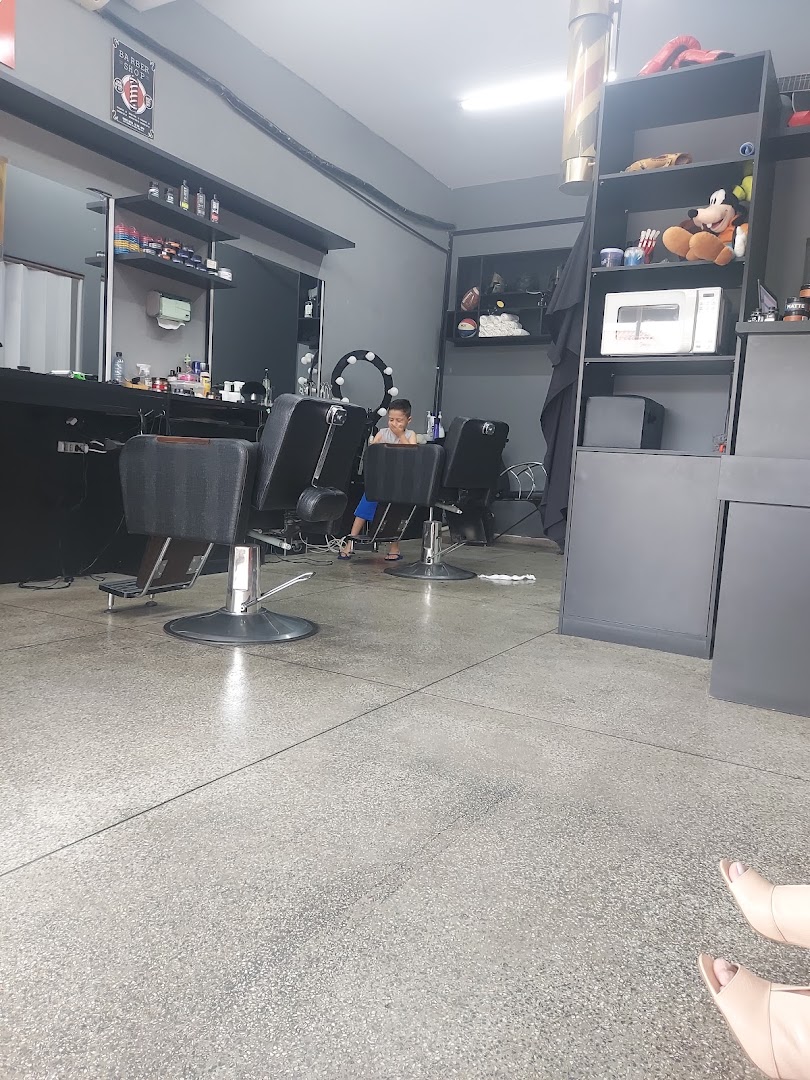 Criança em pé ao lado das cadeiras de barbeiro na Barbearia Moruk, esperando o corte