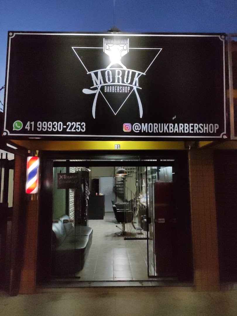 Fachada da Barbearia Moruk iluminada à noite, com letreiro Moruk Barbershop e poste de barbeiro na entrada